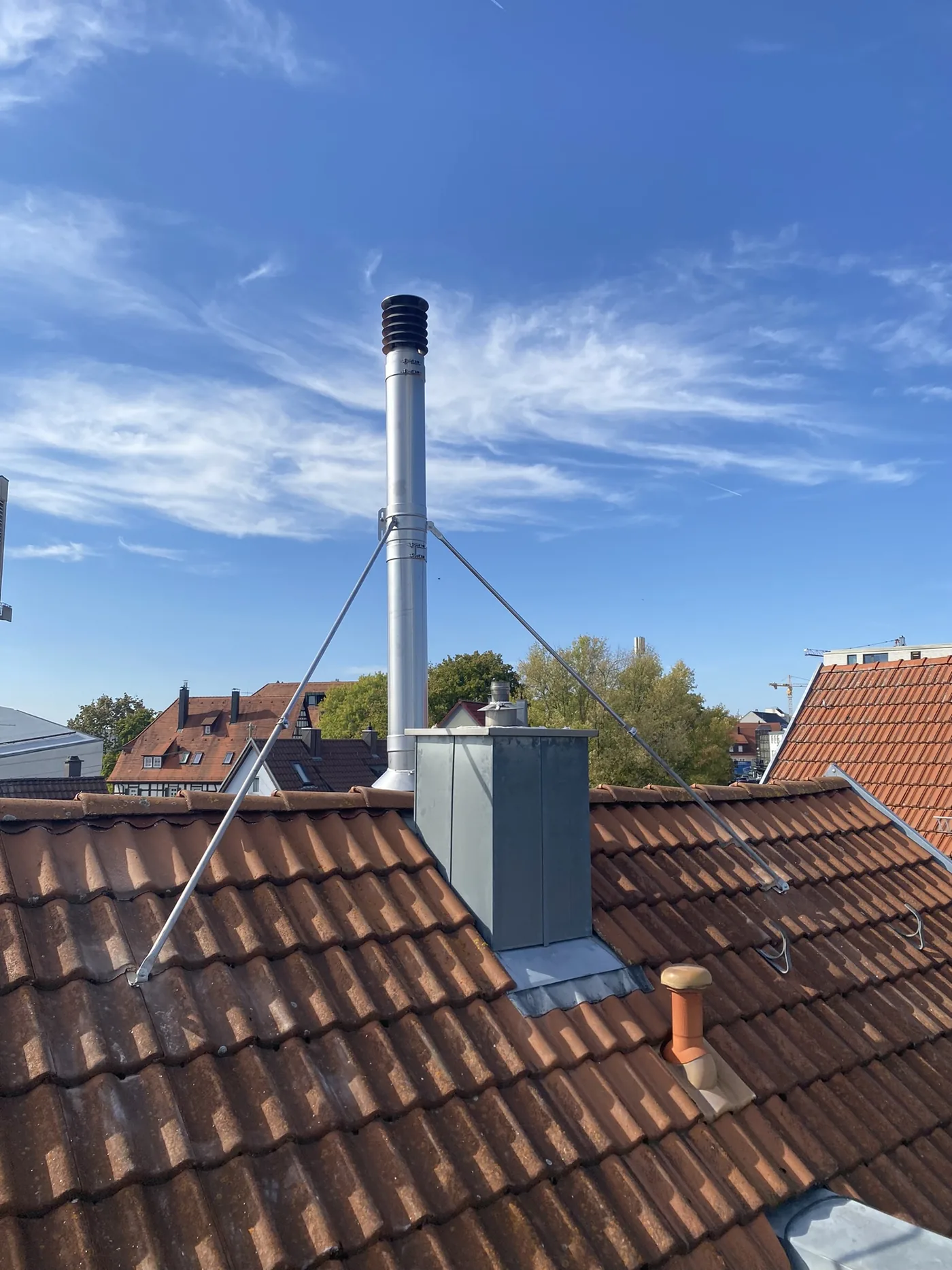 Edelstahlschornstein mit Abspannung über einem Ziegeldach